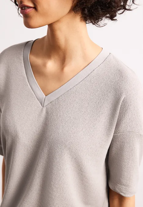 Frau mit lockigem Haar in hellgrauem V-Ausschnitt-Oberteil mit kurzen Ärmeln.