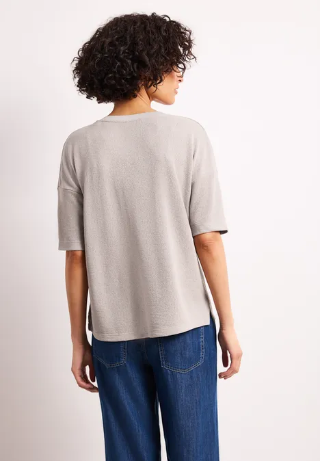 Rückansicht einer Person mit krausem Haar, sie trägt ein hellgraues T-Shirt und blaue Jeans vor weißem Hintergrund.