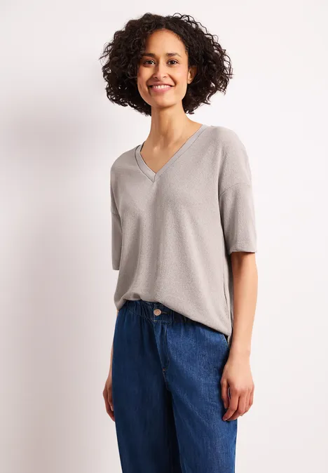 Frau trägt graues V-Pullover-Shirt mit halblangen Ärmeln und blaue High-Waist-Jeans.