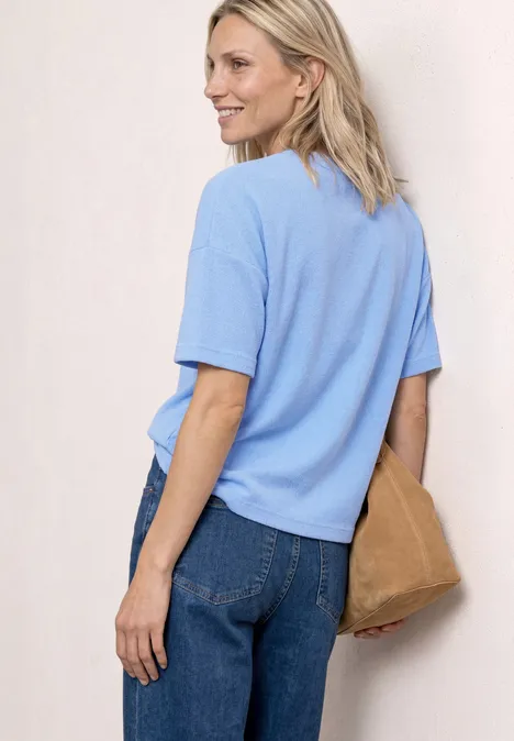 Frau von hinten in hellblauem T-Shirt, Jeans und mit brauner Handtasche.