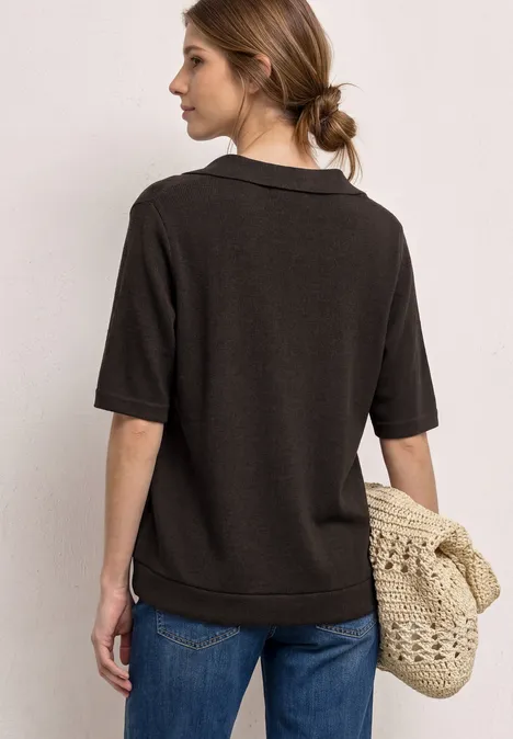 Vrouw van achteren in een donker polohemd, spijkerbroek en gevlochten tas