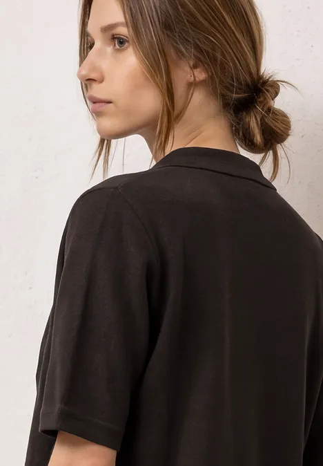 Jonge vrouw met samengebonden haar draagt een zwart T-shirt met korte mouwen en kijkt opzij.