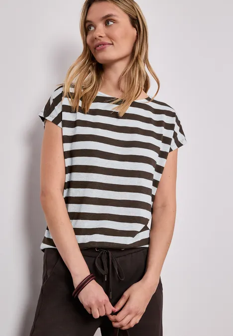 Vrouw in zwart-wit gestreept shirt en zwarte broek voor een neutrale achtergrond.