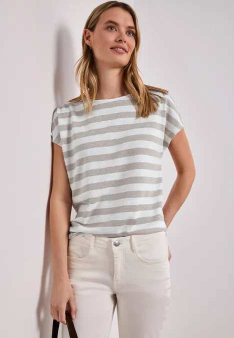 Vrouw in gestreept shirt en lichte broek, staat ontspannen met handen in de zakken.