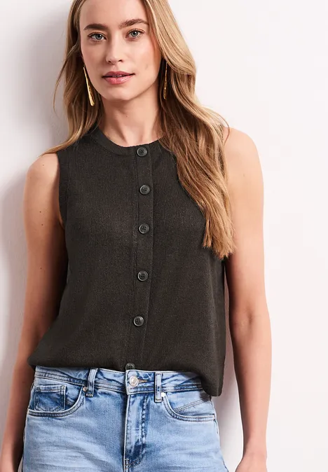 Frau in ärmelloser schwarzer Bluse mit Knopfleiste und blauer Jeans.