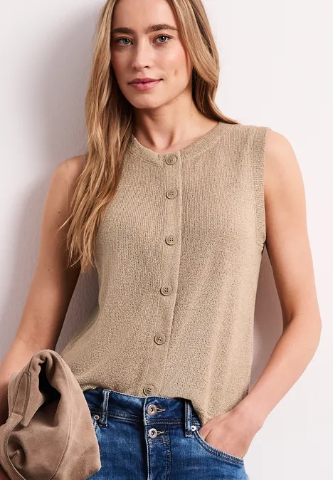 Ärmelloses Top in Beige mit Knopfleiste, locker geschnitten, zu Jeans getragen, Jacke über dem Arm.