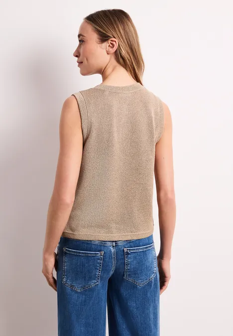 Rückenansicht einer Frau in ärmellosem beigem Top und blauen Jeans.