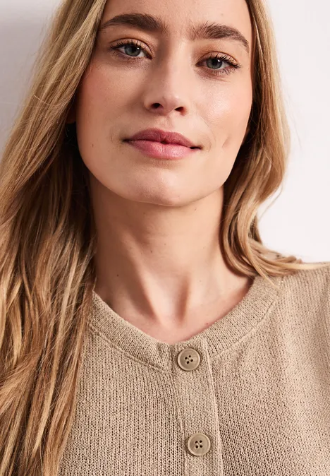 Eine Person mit langem Haar trägt einen beigen, gestrickten Pullover mit Knöpfen.