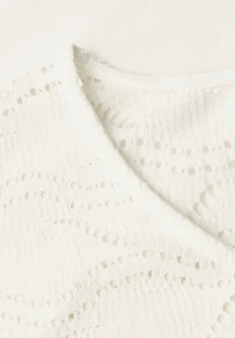 Nahaufnahme einer cremeweißen gehäkelten Bluse mit V-Ausschnitt und Wellenmuster.