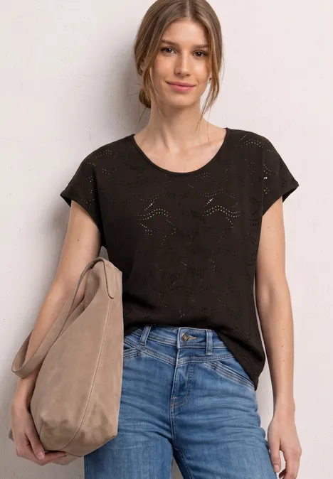 Frau trägt schwarzes T-Shirt, blaue Jeans und hält eine beige Tasche.