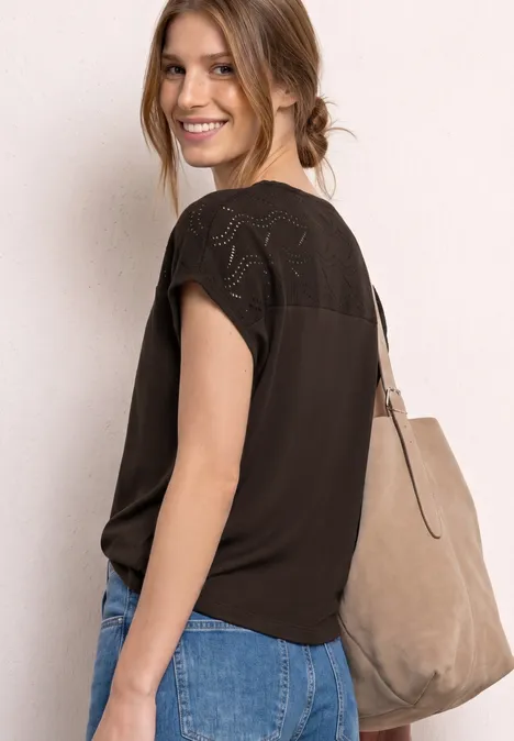 Frau in schwarzem Spitzen-Oberteil, Jeans und beiger Tasche über der Schulter, seitliche Ansicht.