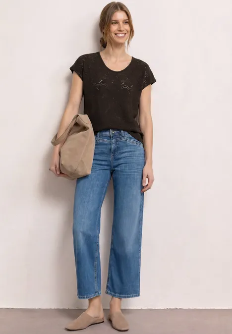 Frau in schwarzem T-Shirt, weiter blauer Jeanshose, beiger Tasche und flachen Schuhen