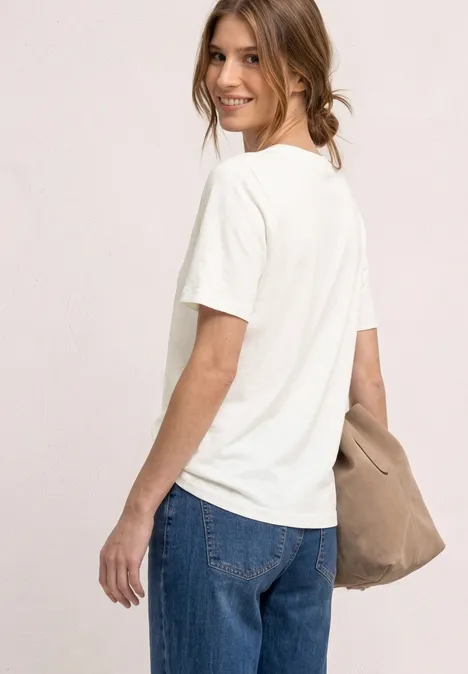 Eine Person ist von hinten zu sehen, trägt ein weißes T-Shirt, blaue Jeans und eine beige Tasche.