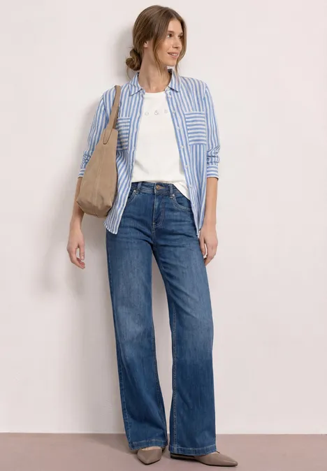 Frau in weißem T-Shirt, blauer gestreifter Hemdbluse, weiten Jeans und beiger Schultertasche