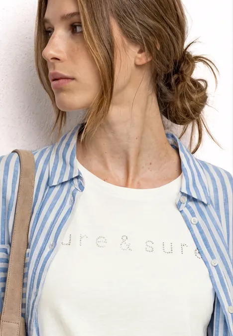 Junge Frau mit Hochsteckfrisur, weißem T-Shirt und blau-weiß gestreiftem Hemd, seitlich schauend.