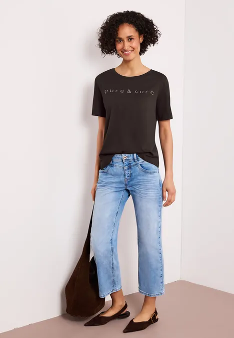 Vrouw met zwart bedrukt T-shirt, lichtblauwe jeans en zwarte ballerina’s, met een bruine tas