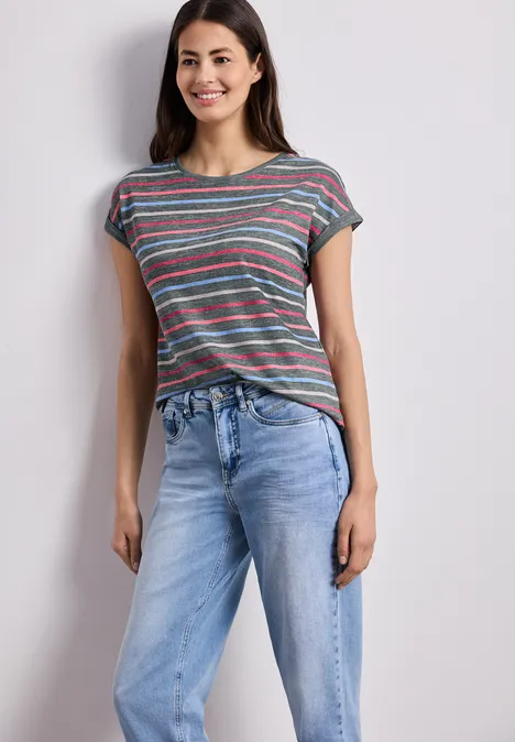 Frau in gestreiftem T-Shirt und blauen Jeans vor neutralem Hintergrund.