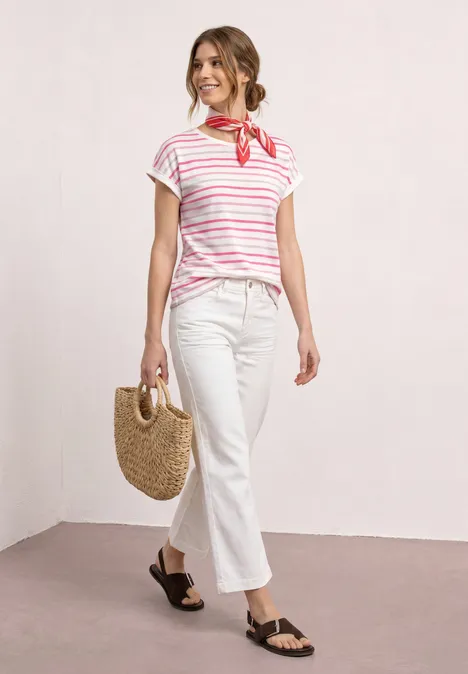 Vrouw in gestreept T-shirt, witte broek, rode halsdoek, strooien tas en zwarte sandalen.