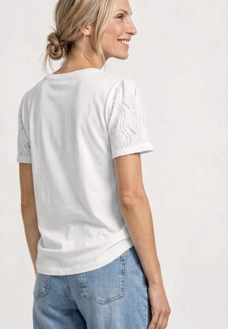 Frau von hinten und seitlich, trägt weißes T-Shirt mit strukturierten Ärmeln, Haare locker zum Dutt gebunden.