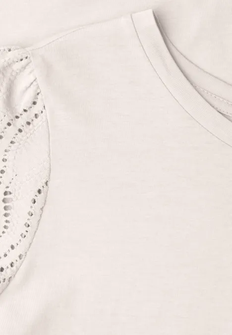 Hellbeiges T-Shirt mit Rundhalsausschnitt und mit funkelnden Nieten verzierten Ärmeln.