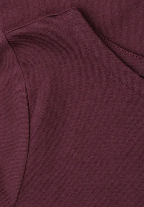 Nahaufnahme einer aufgesetzten Tasche an einem weinroten Kapuzenpullover.