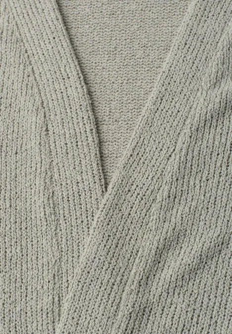 Nahaufnahme eines grauen, gestrickten Cardigans mit überkreuztem V-Ausschnitt.