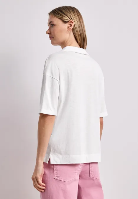 Frau von hinten in lockerem weißen Kurzarm-Polo mit Kragen und rosafarbenen Hosen.