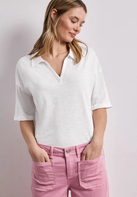 Frau in weißem Poloshirt und pinken Jeans mit aufgesetzten Taschen.