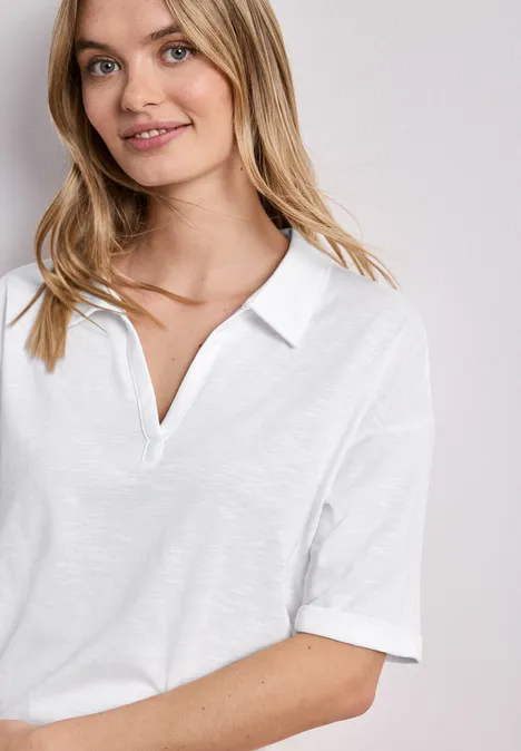 Jonge vrouw in wit poloshirt, glimlachend voor een neutrale achtergrond.