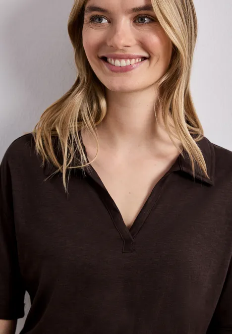 Frau mit schulterlangem blondem Haar und dunkelbraunem V-Shirt vor hellem Hintergrund.