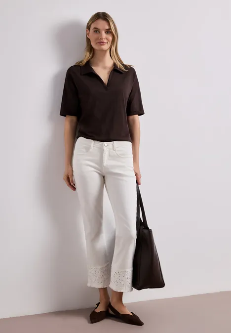 Eine Frau trägt ein schwarzes kurzärmeliges Oberteil, weiße Spitzenhose, schwarze Ballerinas und eine schwarze Tasche.