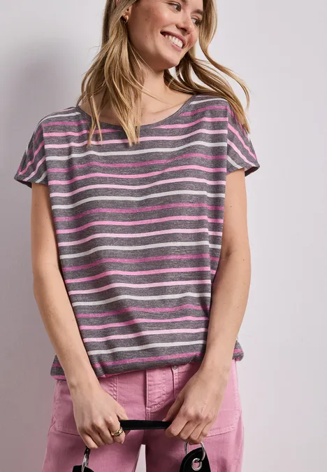 Eine Frau trägt ein grau-rosa gestreiftes T-Shirt und rosa Shorts und hält einen schwarzen Gurt.