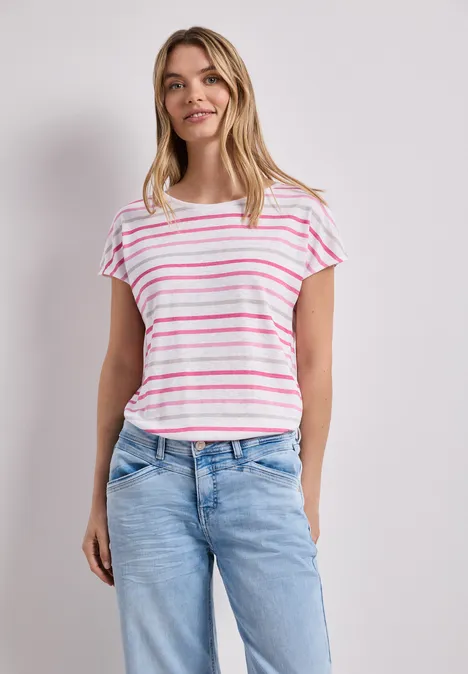 Frau trägt weißes T-Shirt mit rosa Streifen und blaue Jeans vor neutralem Hintergrund.
