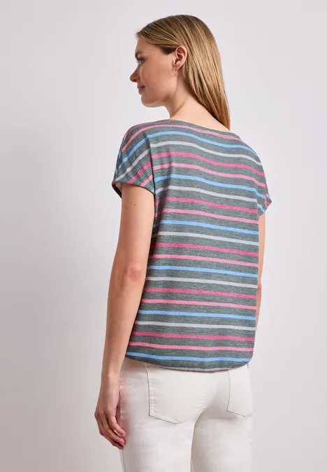 Frau mit buntem, quer gestreiftem T-Shirt im Profil vor hellem, neutralem Hintergrund.