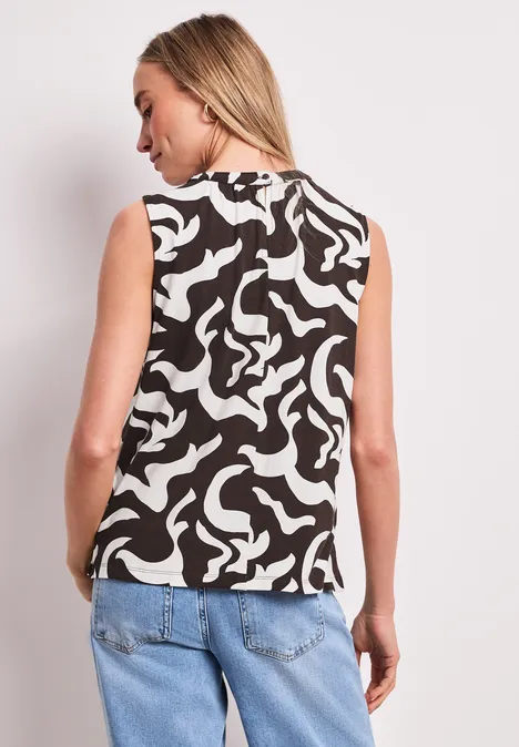 Femme de dos portant un débardeur noir et blanc à motif abstrait et un jean bleu.