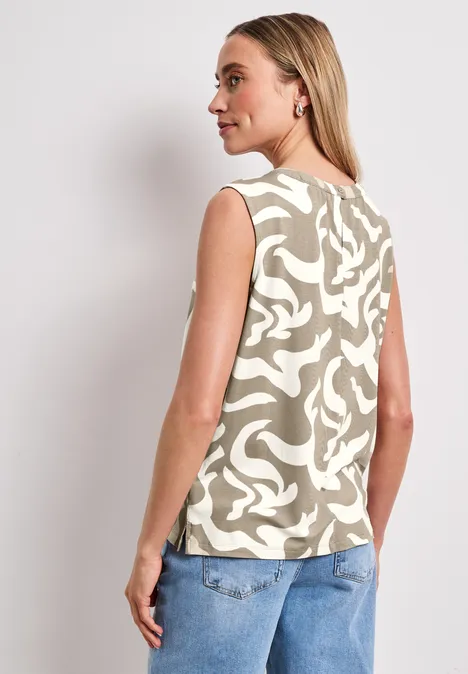 Vrouw van achteren in een mouwloos beige top met wit motief en een blauwe jeans.