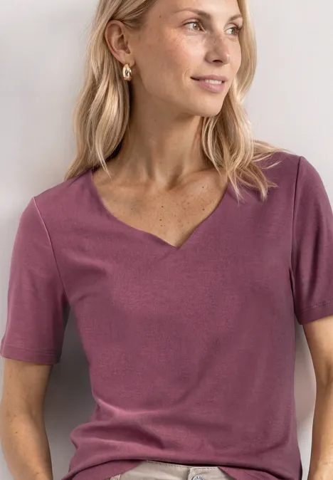 Basic T-Shirt mit Herzausschnitt dark clouded blush Eine Frau trägt ein kurzärmeliges, violettes V-Neck-Shirt, Nahaufnahme vom Oberkörper.