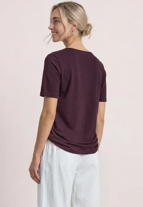 Basic T-Shirt mit Herzausschnitt rustic rouge Eine Frau von hinten mit lila T-Shirt und weißer Hose, die lächelnd zur Seite schaut.