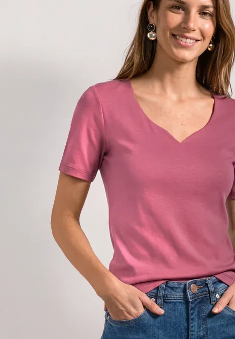 Basic T-Shirt mit Herzausschnitt blush berry Lächelnde Frau mit rosa T-Shirt und Jeans, Hände in den Taschen.