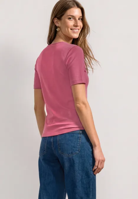 Basic T-Shirt mit Herzausschnitt blush berry Eine Frau in einem pinken T-Shirt und blauen Jeans steht seitlich mit Blick über die Schulter.
