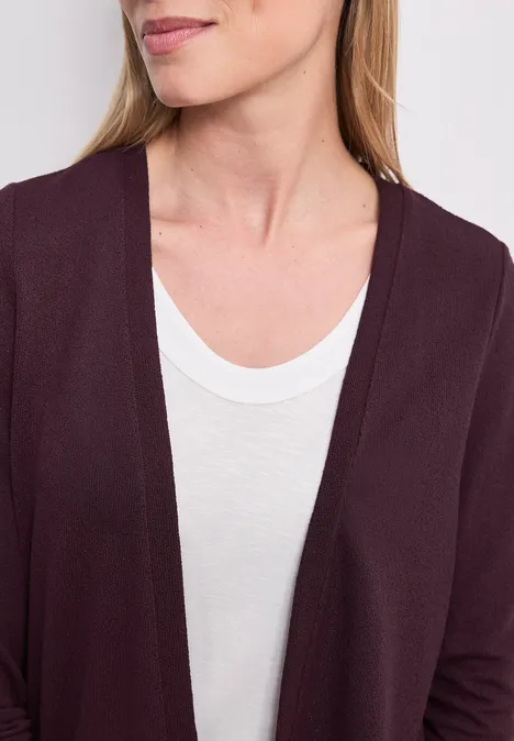 Eine Frau trägt ein weißes T-Shirt und einen bordeauxroten Cardigan.