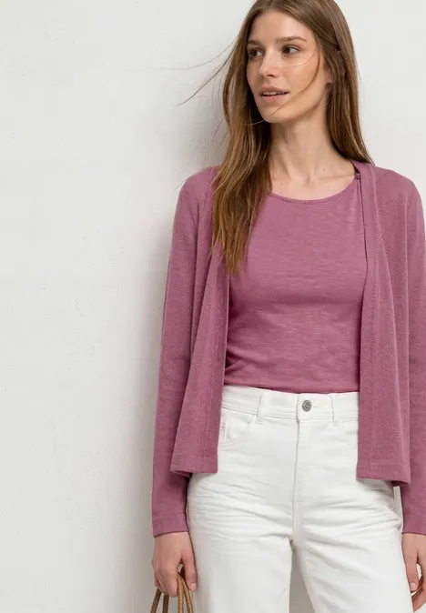 Veste à manches longues en look tricot dark clouded blush Une femme porte un top rose et un gilet assorti avec un pantalon blanc, debout devant un mur blanc.