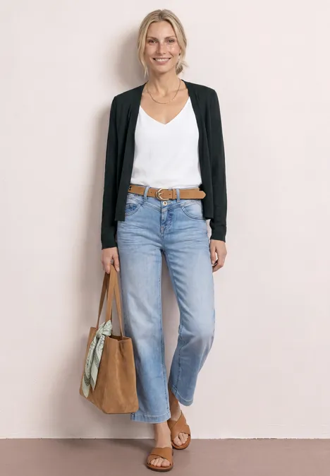 Frau trägt weiße Bluse, schwarze Strickjacke, helle Cropped-Jeans, braune Sandalen und große Tasche.