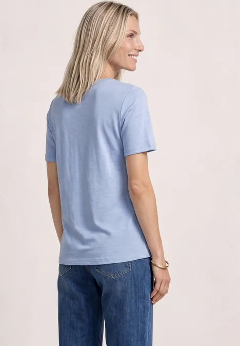Eine von hinten gesehene Person mit blonden Haaren, die ein hellblaues T-Shirt und Jeans trägt.