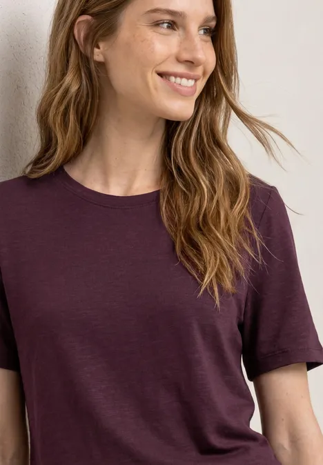 Femme aux longs cheveux blonds portant un t-shirt violet simple jusqu'à la taille.