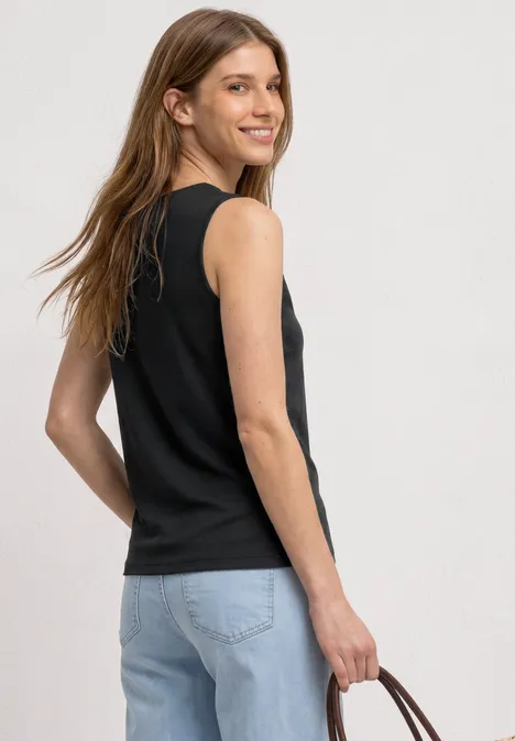 Top mit Rundhals und Cut-Out-Detail Black Frau im Halbprofil trägt schwarzes ärmelloses Top, blaue Jeans und hält eine braune Handtasche.