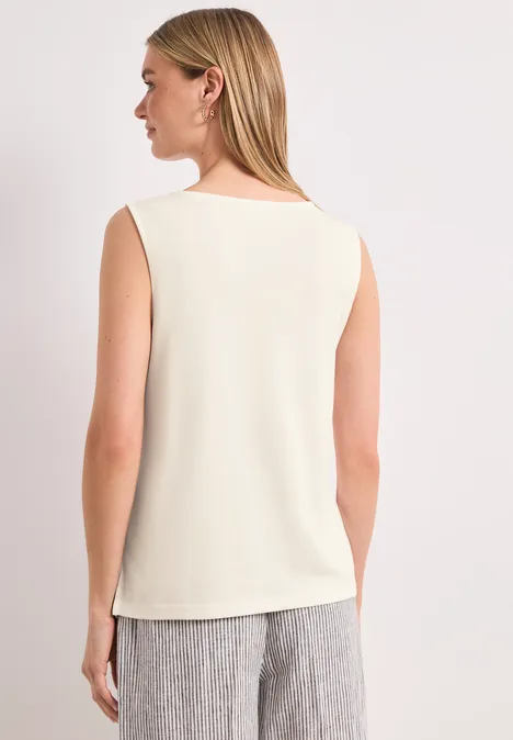 Vrouw van achteren in een mouwloos crèmekleurig topje en grijze broek.