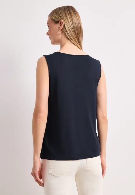 Vrouw van achteren in een zwart mouwloos topje en witte broek.