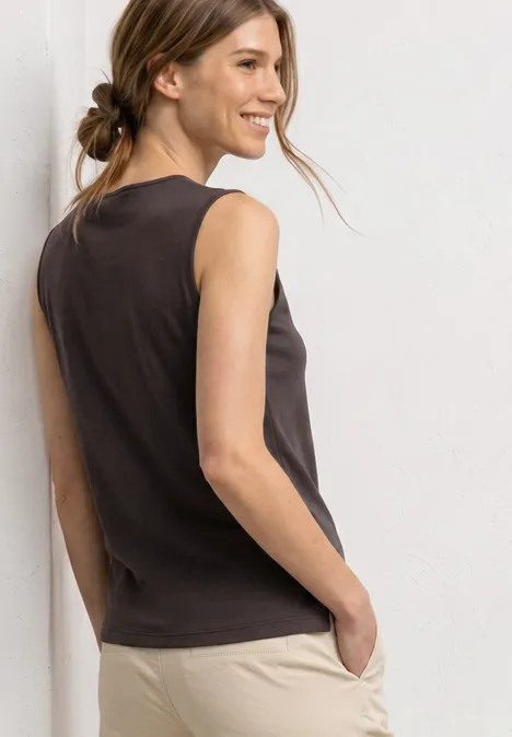Femme vue de dos portant un top sans manches gris foncé et un pantalon beige, cheveux attachés en chignon décontracté.