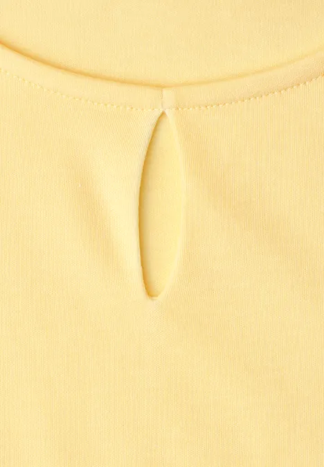 Close-up van een geel shirt met een sierlijk druppelvormig splitje in de nek.
